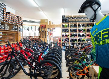 Fahrradladen mit Reihen von Mountainbikes, Regal mit Fahrradhelmen und Schaufensterpuppe in Sportkleidung.