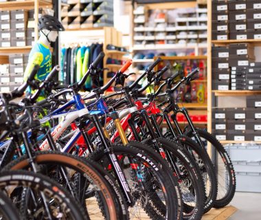In einem Fahrradgeschäft stehen mehrere Fahrräder in einer Reihe. Im Hintergrund sind Regale mit Schuhkartons und Zubehör.