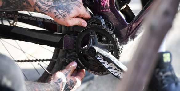 Eine tätowierte Hand repariert ein Fahrrad, während sie an der Kettenblatt- und Schaltmechanik arbeitet.