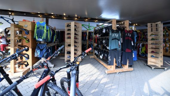 Fahrradladen mit Mountainbikes, bunter Sportkleidung und Zubehör auf Holzregalen.