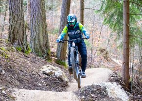 Person mit Helm fährt auf Mountainbike durch bewaldeten Pfad im Wald.