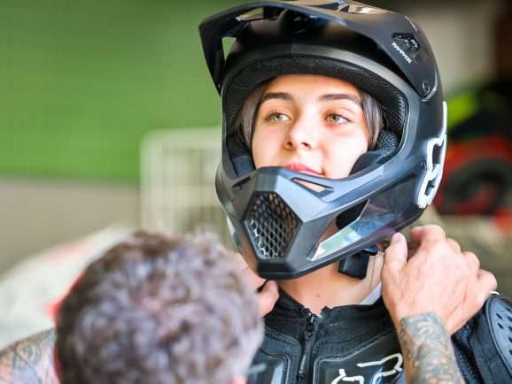 Person trägt einen schwarzen Motorradhelm, andere Person hilft beim Anpassen.