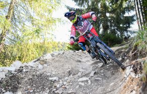 Ein Mountainbiker fährt mit hoher Geschwindigkeit einen schmalen, steinigen Pfad durch einen Wald.