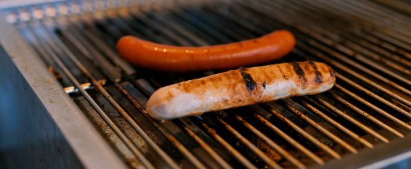 Zwei Würste auf einem Grillrost, eine braun, die andere mit Grillstreifen.